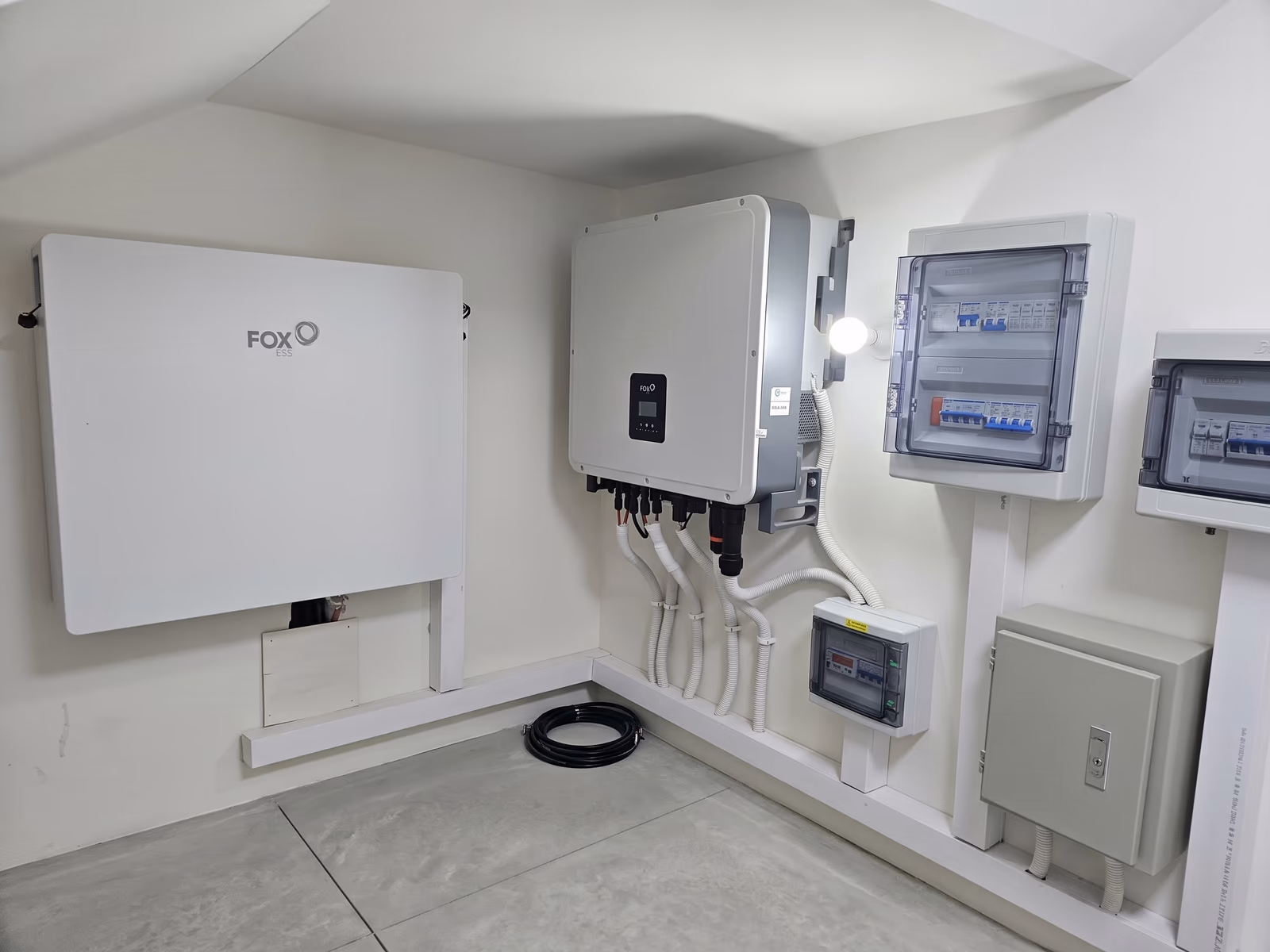 FOX ESS battery, three-phase hybrid inverter and protection enclosures along the walls of an under-stair plant room