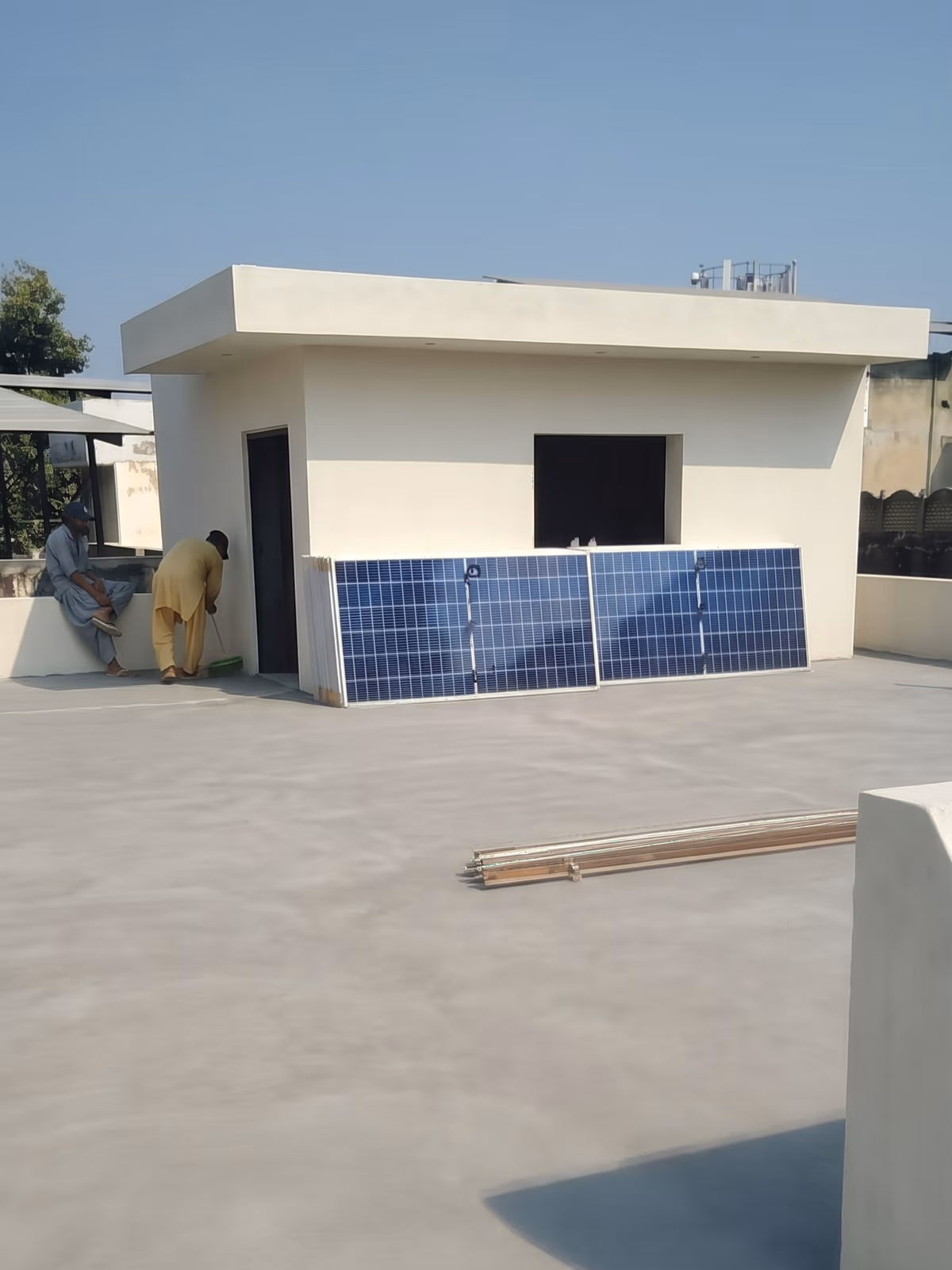 Solar modules staged in front of the rooftop room on the bare concrete roof